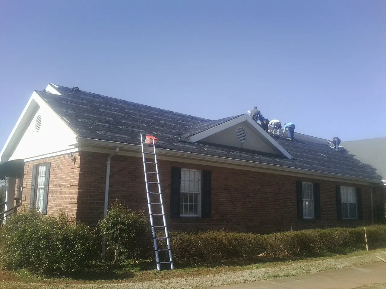 Crew tearing shingles off a brick ranch roof with a ladder set — Metal Roof Repair work by our crew in Yellville