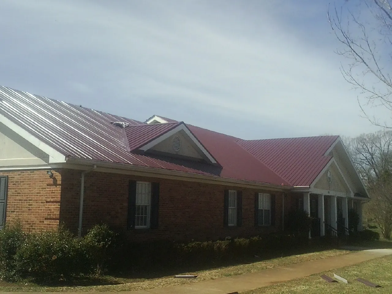 Red metal roof with gabled entries on a long brick building, from a Hail Damage Roof Repair job in Yellville