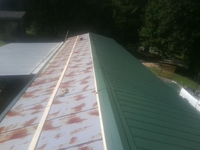 Old rusted panels beside newly installed green metal roofing — Wind Damage Roof Repair by Roofing Brothers in Yellville