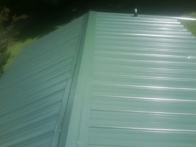 New green metal panels meeting at the ridge of a roof — Flat Roof Repair work by our crew in Yellville