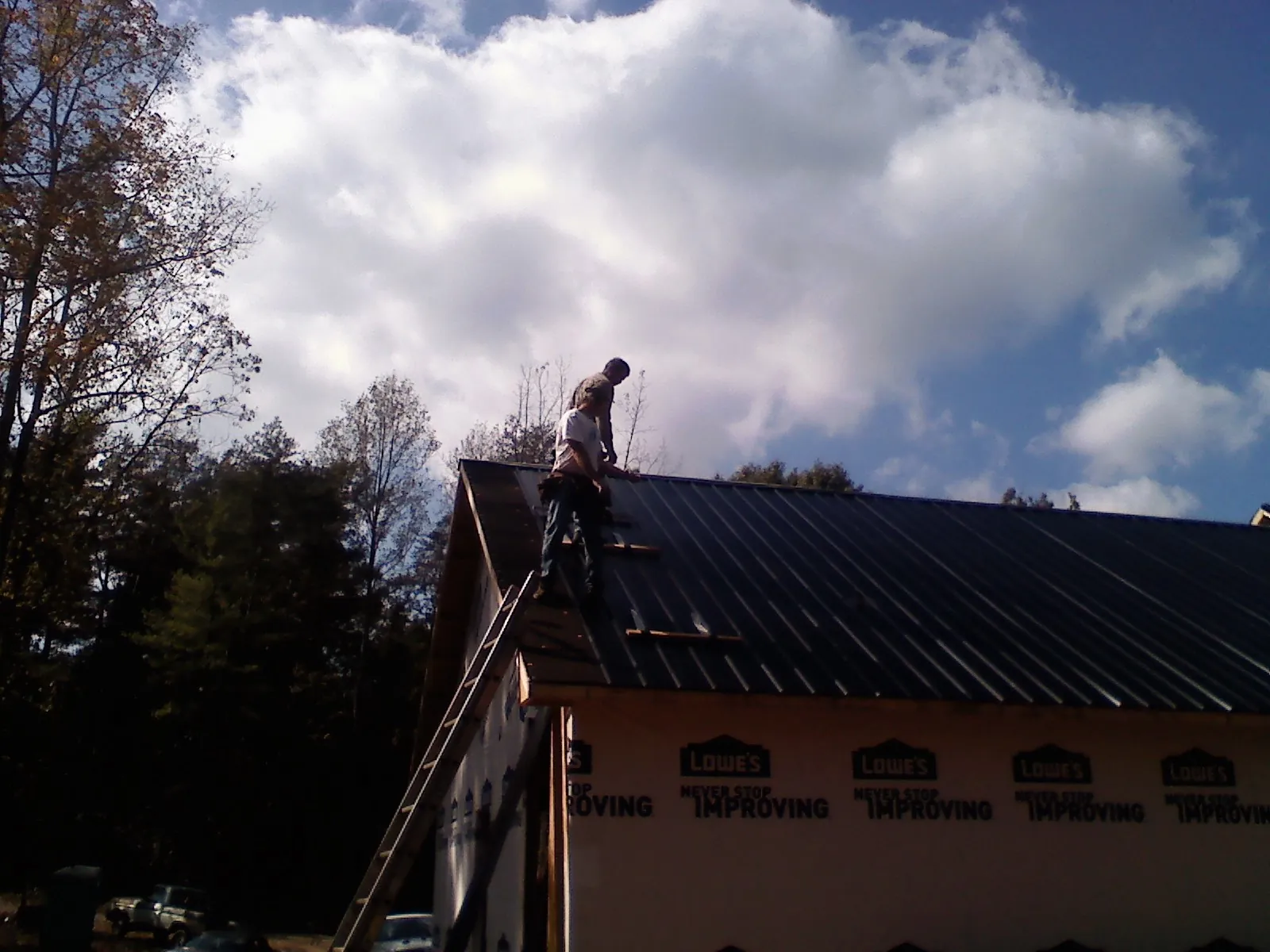 Roofer fastening dark metal panels high against a cloudy sky in Yellville