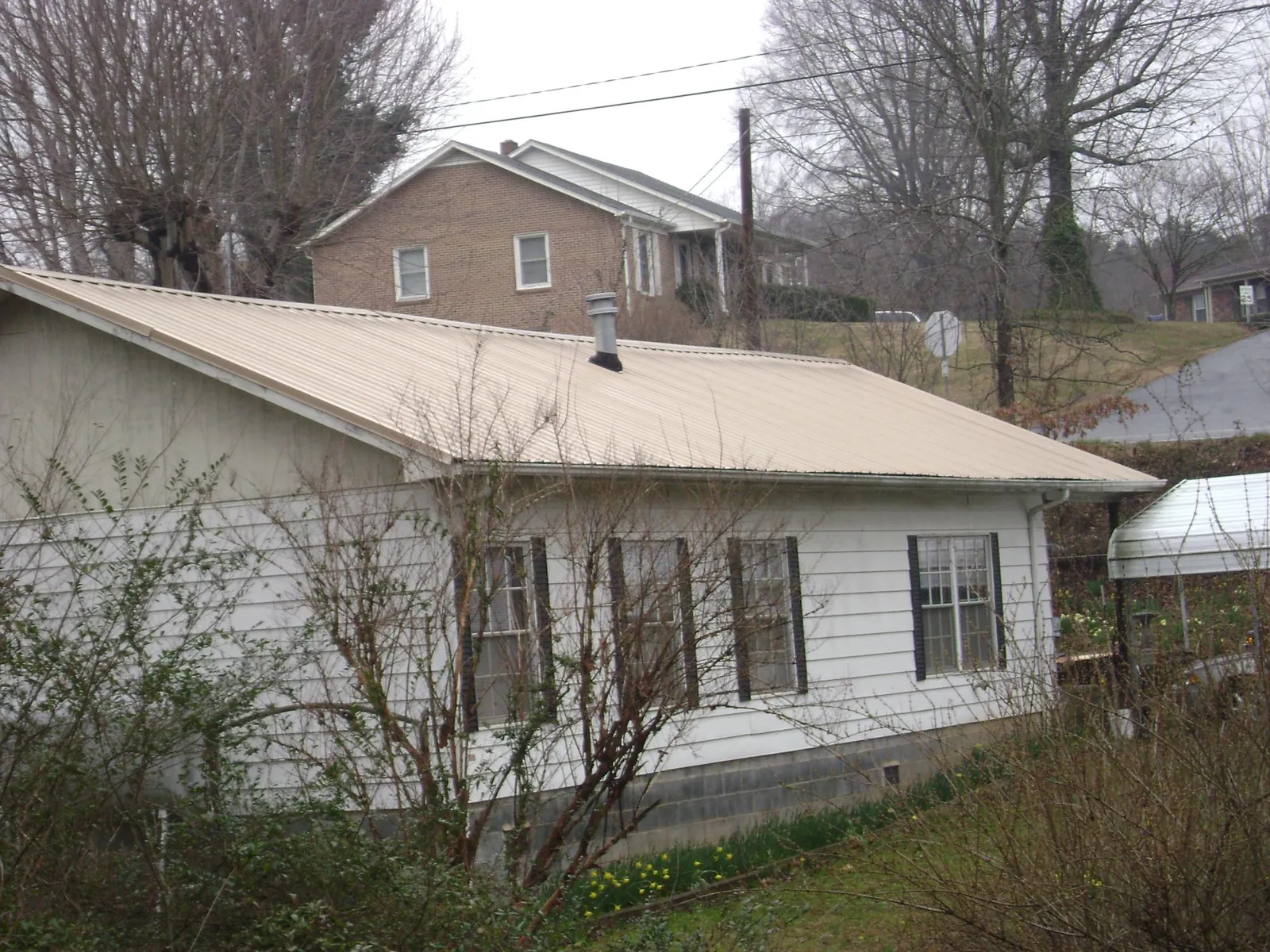 Tan metal roof on a white sided house set into a hillside — Commercial Roofing by Roofing Brothers in Yellville