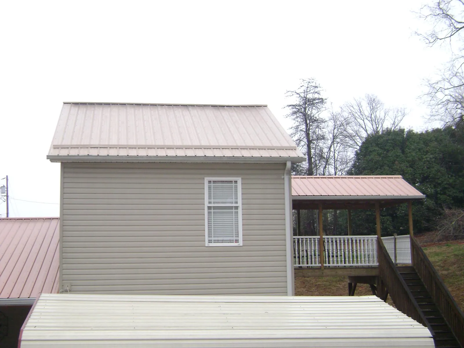 Tan metal roofs on a two story addition and attached porch, from a Roof Replacement job in Yellville